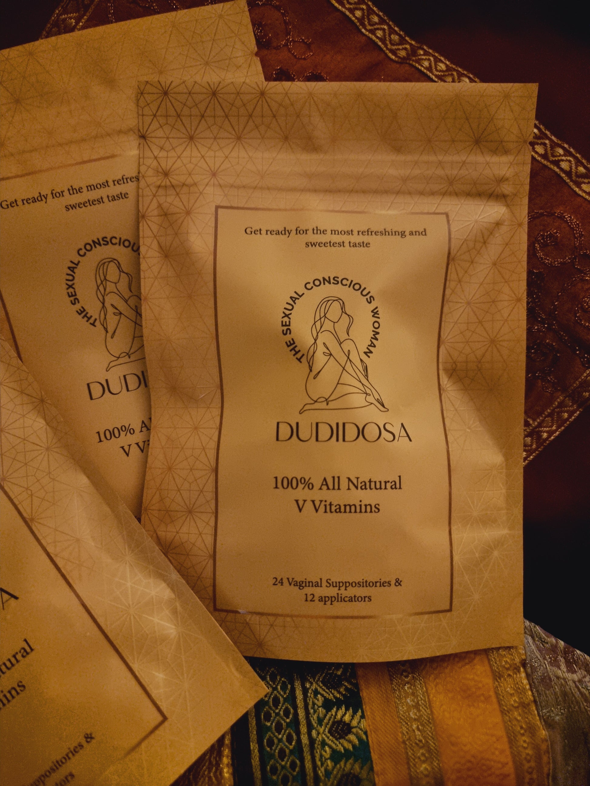 DUDIDOSA V-Vitamins pouches lying on colorful silk fabric. The warm, rich setting gives a cozy and elegant feel — highlighting the product’s natural, gentle formula that helps balance pH, improve freshness, and subtly sweeten taste.